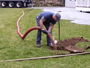 Septic pumping technician servicing a residential septic tank with a vacuum hose in Worcester, MA