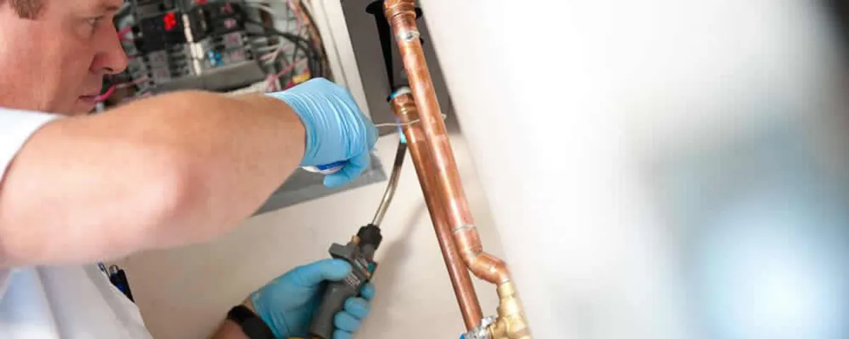 Water heater repair technician testing copper pipe connections and controls in Worcester, MA